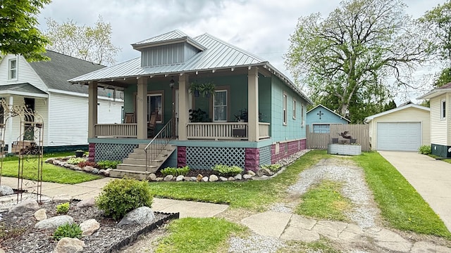 view of front of house with driveway, a porch, a detached garage, an outdoor structure, and metal roof