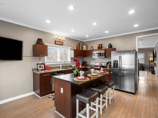 kitchen featuring stainless steel appliances, a breakfast bar area, light wood-style flooring, crown molding, and a center island