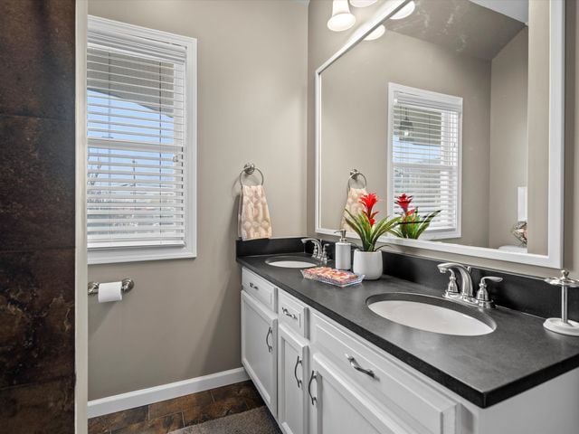 bathroom with baseboards, double vanity, and stone finish floors