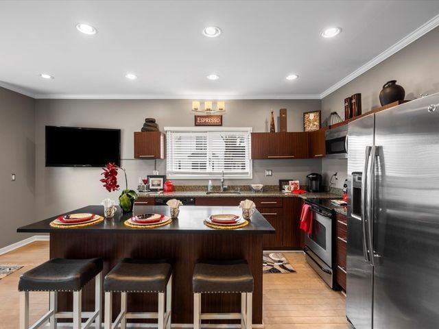 kitchen with stainless steel appliances, a kitchen bar, a sink, dark countertops, and ornamental molding