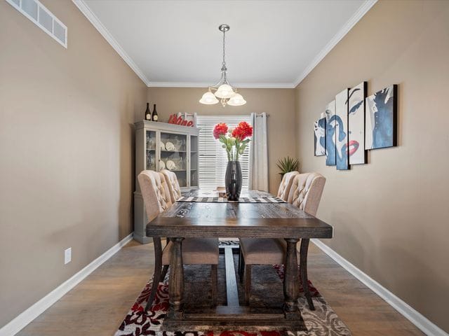dining area featuring a chandelier, wood finished floors, crown molding, and baseboards