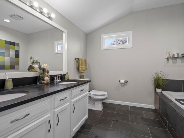 1106 Bennaville Ave, Birmingham, MI 48009 - bathroom with lofted ceiling, toilet, double vanity, tiled tub, and baseboards