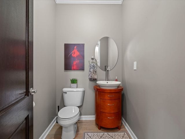 half bathroom featuring toilet, baseboards, vanity, wood finished floors, and ornamental molding
