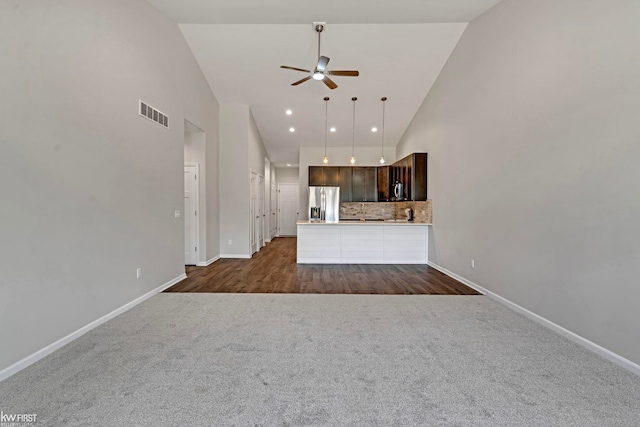 unfurnished living room with high vaulted ceiling, dark carpet, a ceiling fan, and baseboards