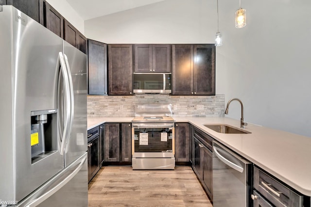 kitchen with stainless steel appliances, a sink, decorative backsplash, light wood finished floors, and vaulted ceiling
