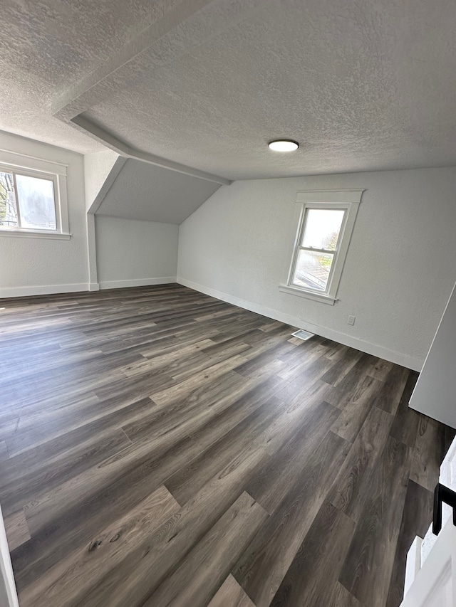 bonus room featuring healthy amount of natural light, dark wood-style flooring, a textured ceiling, baseboards, and vaulted ceiling