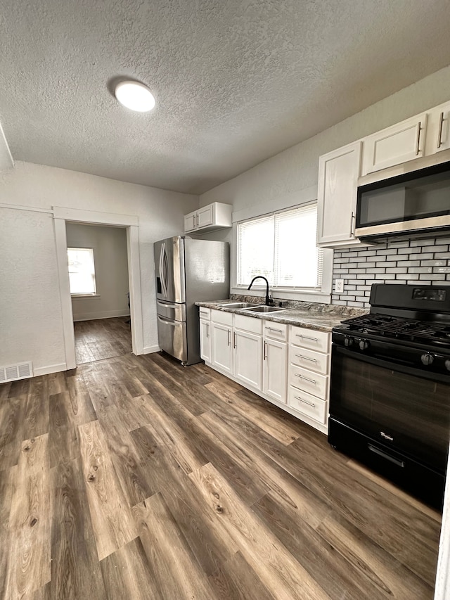 kitchen featuring appliances with stainless steel finishes, a sink, a textured ceiling, plenty of natural light, and white cabinetry
