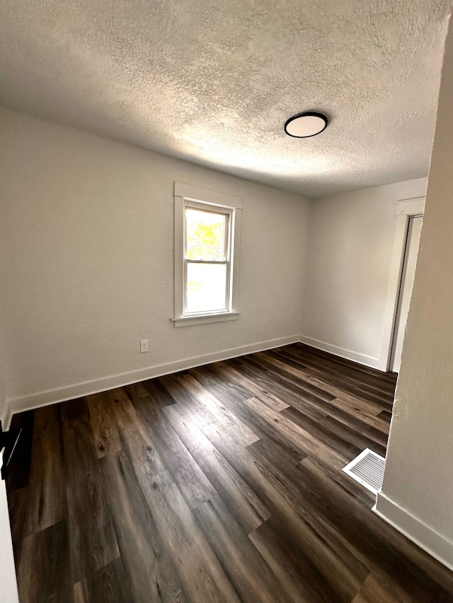 empty room featuring baseboards, a textured ceiling, and dark wood finished floors