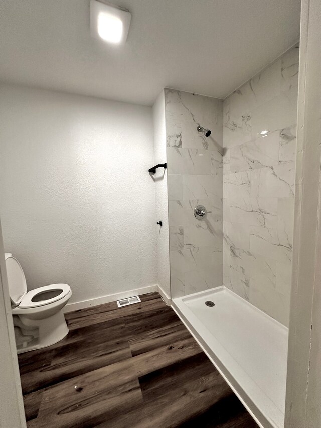 bathroom featuring toilet, a stall shower, baseboards, and wood finished floors