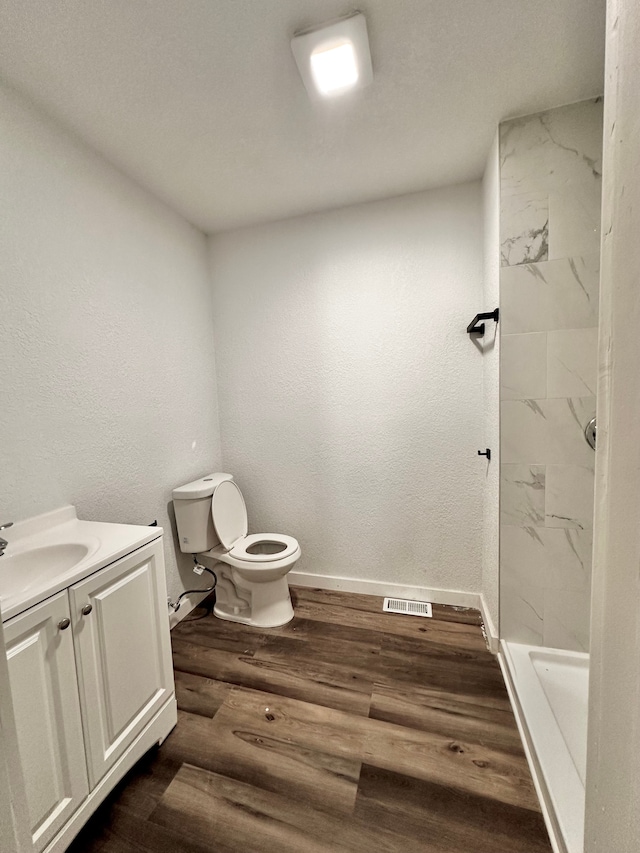 bathroom with toilet, baseboards, wood finished floors, vanity, and a shower