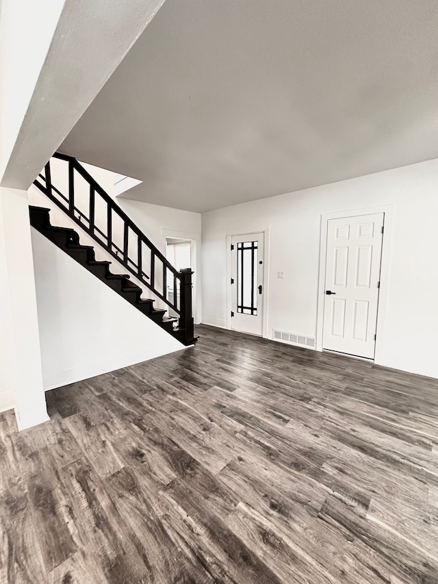 unfurnished living room featuring wood finished floors and stairway