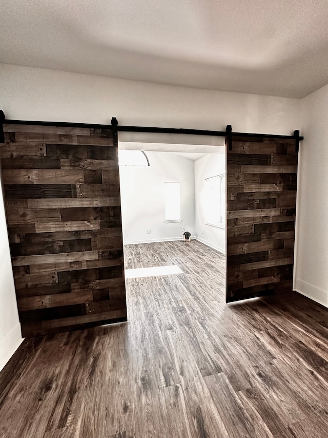 empty room featuring a barn door, wood finished floors, baseboards, and a textured ceiling