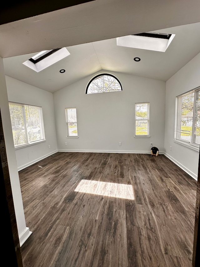 spare room with a skylight, lofted ceiling, dark wood-style floors, and baseboards