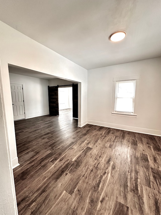 empty room with a barn door, dark wood-type flooring, and baseboards