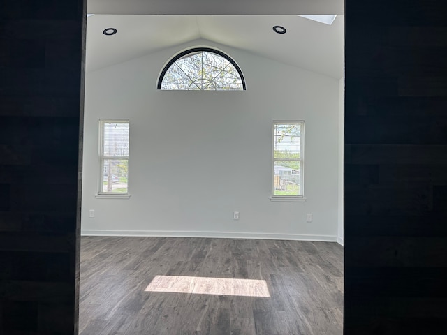unfurnished room featuring healthy amount of natural light, vaulted ceiling, wood finished floors, and baseboards