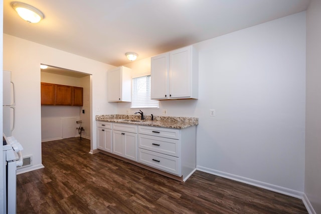 kitchen with dark wood finished floors, a sink, white cabinets, and baseboards