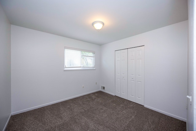 unfurnished bedroom featuring dark colored carpet, baseboards, and a closet
