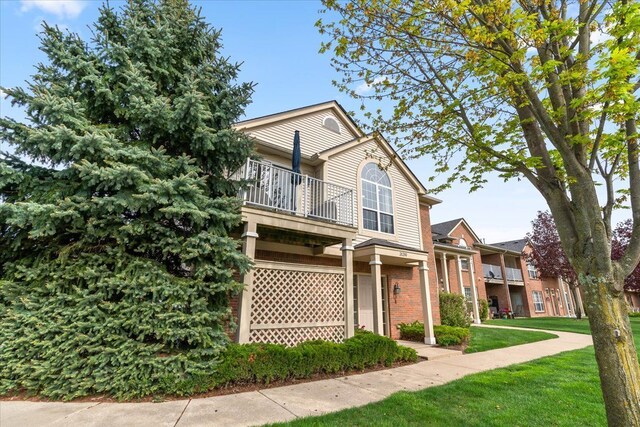 view of front facade with a balcony, a front yard, and brick siding