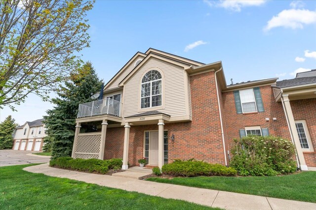 view of front facade featuring a balcony, a front yard, and brick siding
