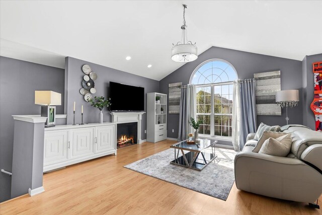 living area featuring lofted ceiling, wood finished floors, and a lit fireplace