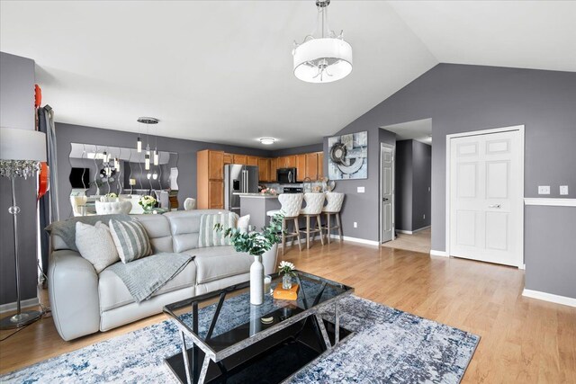 living room with a chandelier, light wood-style flooring, vaulted ceiling, and baseboards
