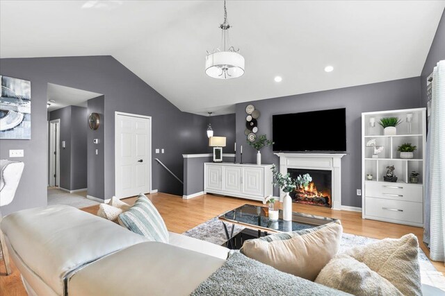 living room with lofted ceiling, light wood-style floors, a lit fireplace, a chandelier, and baseboards