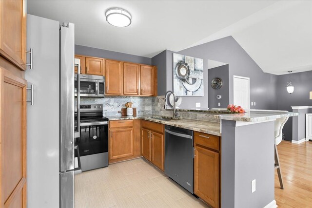 kitchen with stainless steel appliances, a peninsula, a breakfast bar area, backsplash, and a sink