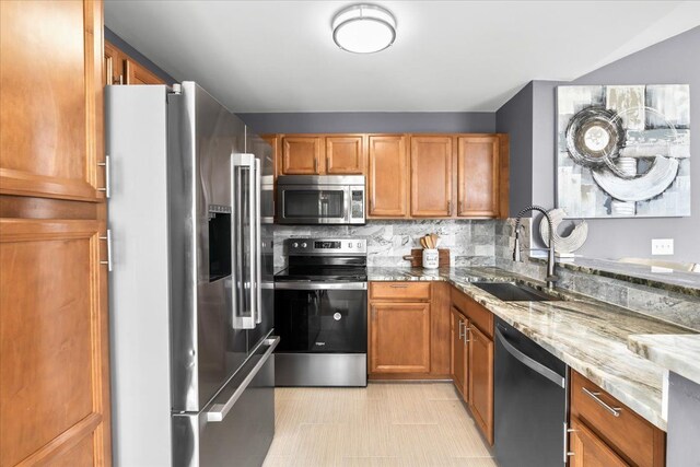 kitchen with appliances with stainless steel finishes, a sink, light stone counters, tasteful backsplash, and brown cabinets