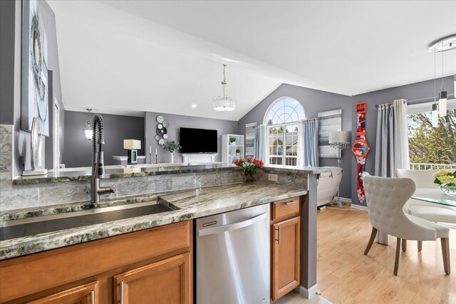 kitchen featuring stainless steel dishwasher, brown cabinets, a sink, vaulted ceiling, and decorative light fixtures
