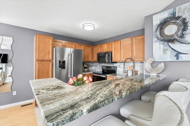 kitchen featuring stainless steel appliances, a peninsula, light stone countertops, backsplash, and light wood finished floors