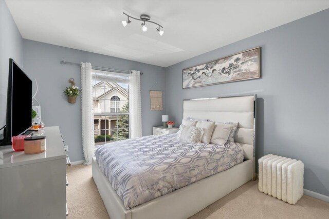 bedroom with radiator heating unit, light colored carpet, baseboards, and track lighting