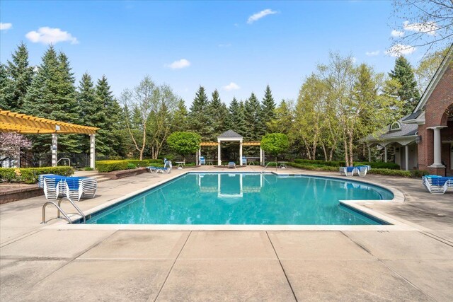 community pool with a patio, a pergola, view of wooded area, and a gazebo