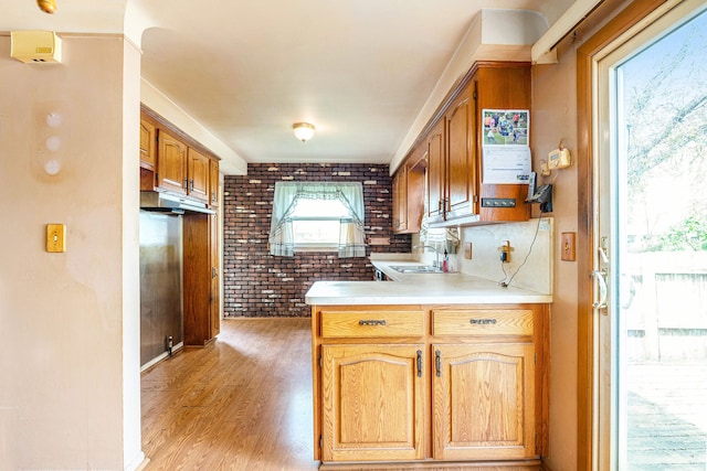 kitchen with a sink, light countertops, brick wall, light wood-style flooring, and a peninsula