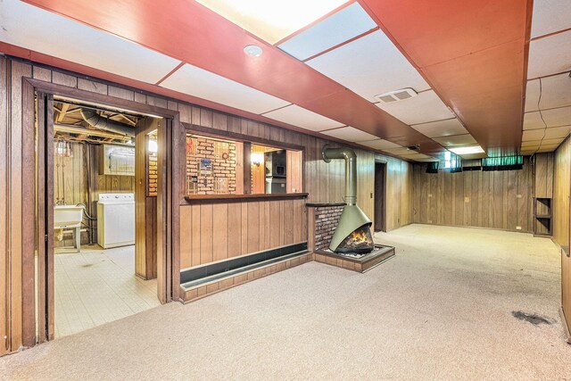 finished basement with washer / dryer, wood walls, a wood stove, carpet, and bar