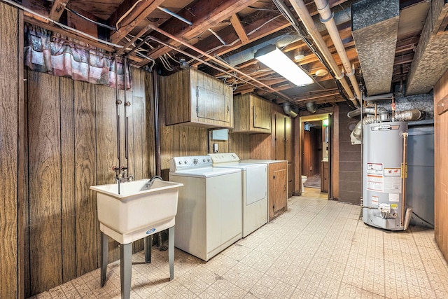 washroom with washer and clothes dryer, water heater, cabinet space, light flooring, and wood walls