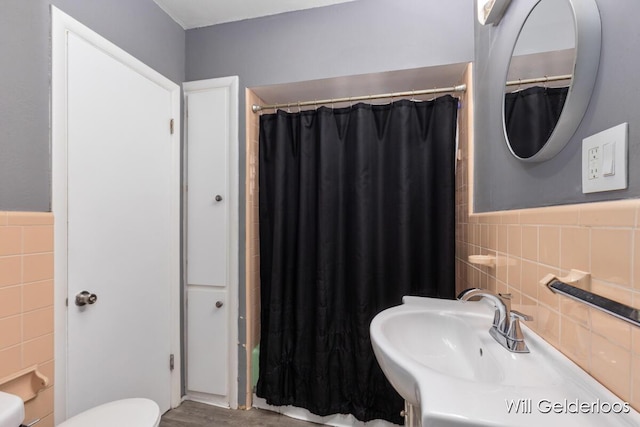 full bathroom with tile walls, a sink, toilet, and a wainscoted wall