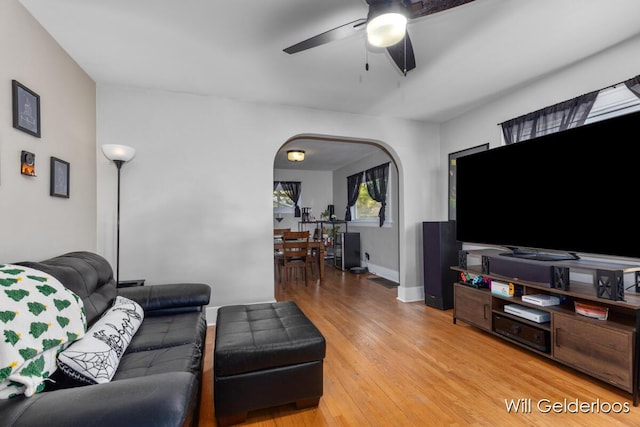 living room with a ceiling fan, light wood-type flooring, arched walkways, and baseboards