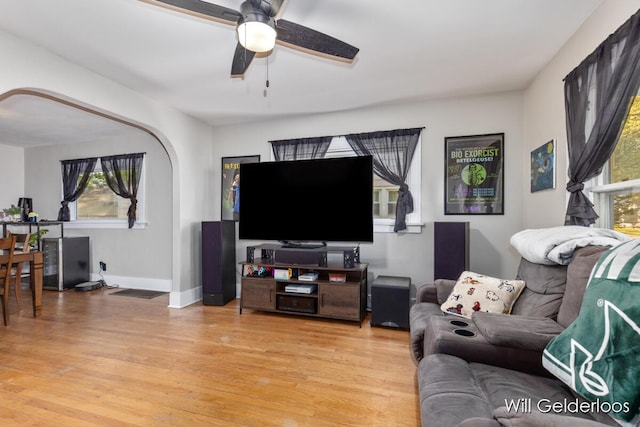 living area with arched walkways, light wood-style flooring, a ceiling fan, and baseboards