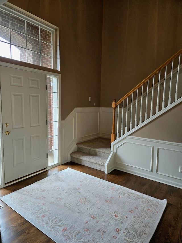 entrance foyer featuring stairway, wainscoting, a decorative wall, and wood finished floors