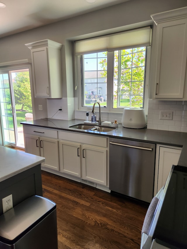 kitchen featuring stainless steel dishwasher, a sink, tasteful backsplash, and dark countertops