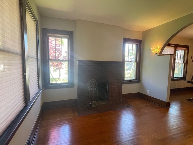 unfurnished living room with arched walkways, plenty of natural light, and wood finished floors