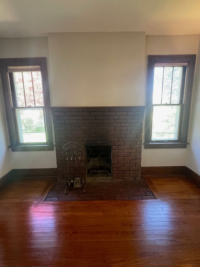 unfurnished living room with healthy amount of natural light, baseboards, a brick fireplace, and wood finished floors