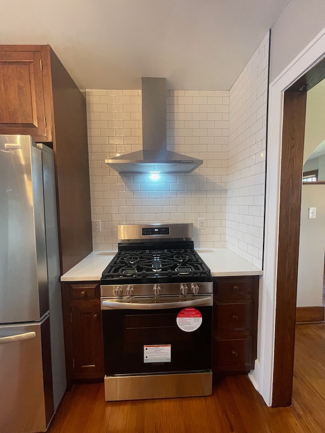 kitchen with stainless steel appliances, wall chimney range hood, light countertops, tasteful backsplash, and dark wood-type flooring