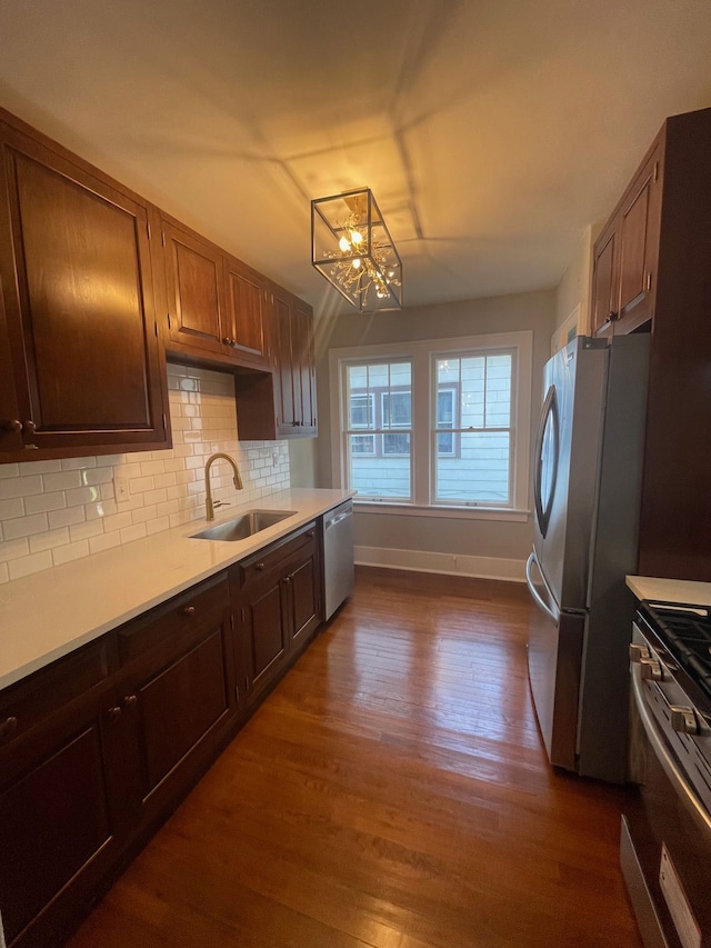 kitchen with a sink, appliances with stainless steel finishes, light countertops, baseboards, and dark wood-type flooring