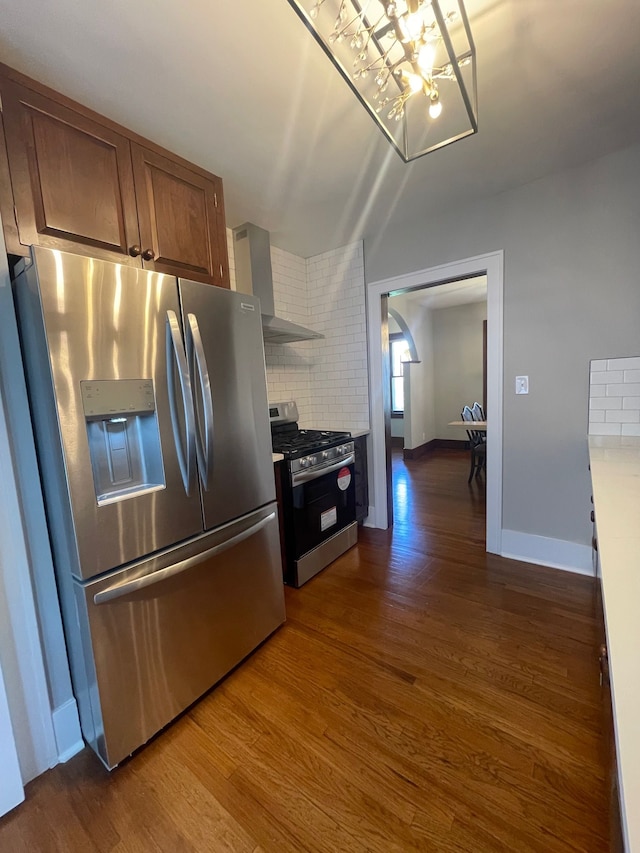 kitchen featuring appliances with stainless steel finishes, wall chimney range hood, dark wood finished floors, a chandelier, and backsplash