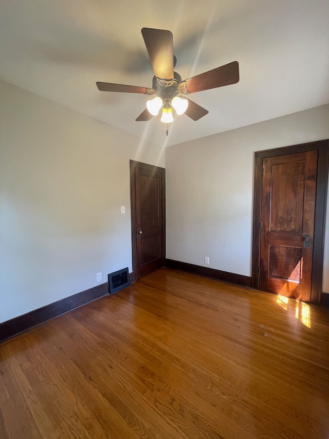 spare room with dark wood-style flooring, a ceiling fan, and baseboards