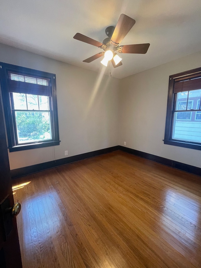 spare room with plenty of natural light, wood finished floors, ceiling fan, and baseboards
