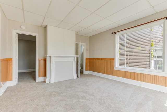 unfurnished living room with a drop ceiling, carpet, a wainscoted wall, and wood walls