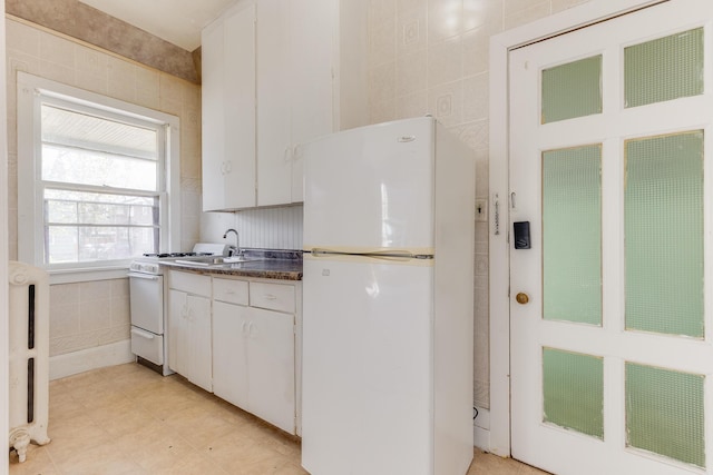 kitchen with white appliances, dark countertops, white cabinets, and tile walls