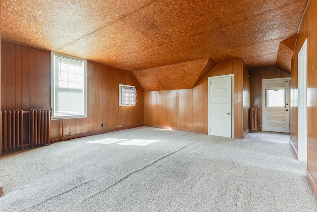 bonus room featuring carpet flooring, radiator, plenty of natural light, lofted ceiling, and wood walls